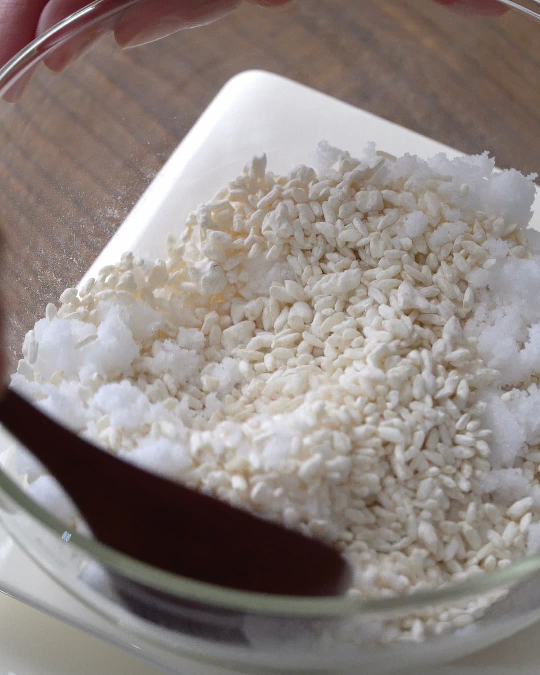 ガラス容器の中で、乾燥米麹と塩を混ぜ合わせる様子
